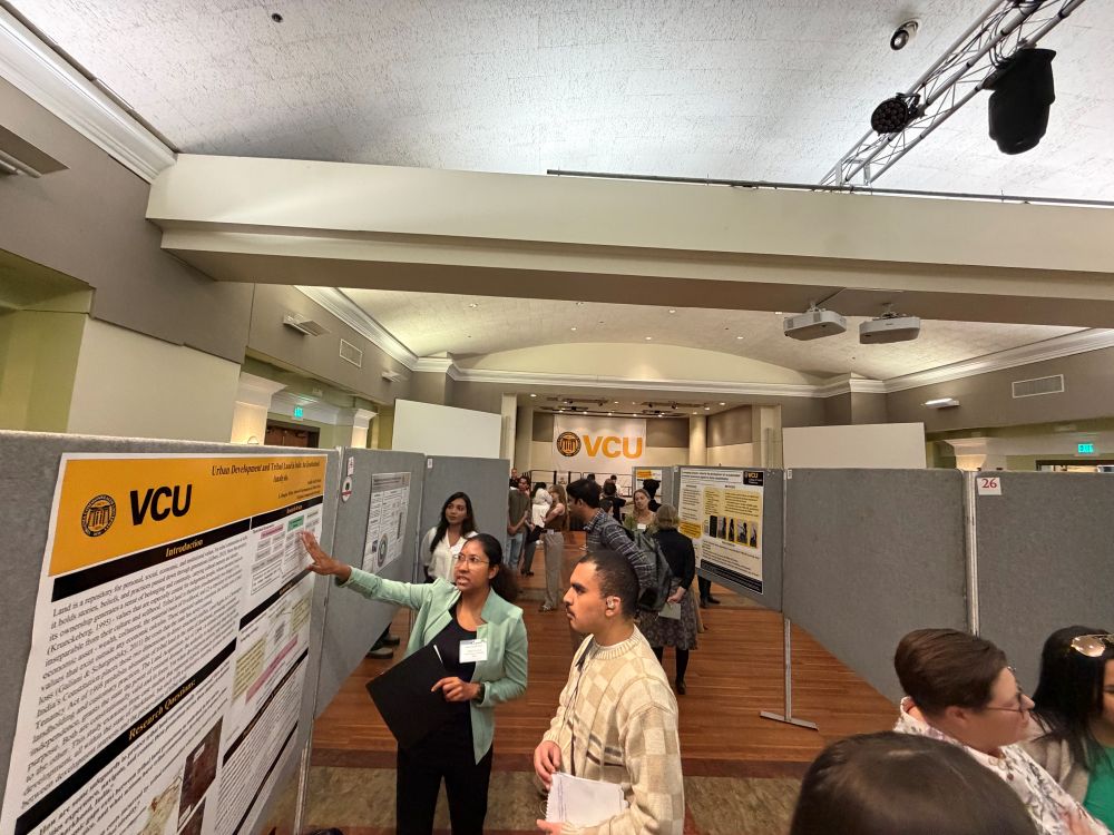 Woman showing off urban dev research poster at grad symposium 2026